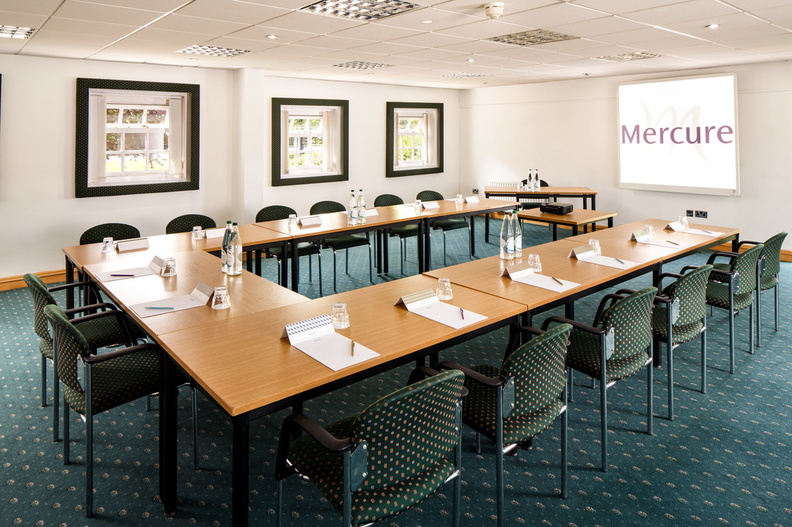 The long table seating 10 in The Boardroom at mercure gloucester bowden hall hotel ready for a meeting, with notepads and bottles of water on the table