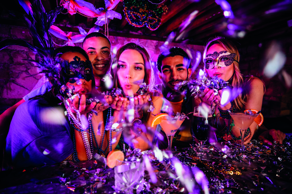 Happy friends celebrating Mardi Gras and blowing confetti at party