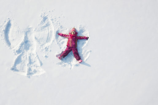 Child girl playing and making a snow angel in the snow. Top flat overhead view