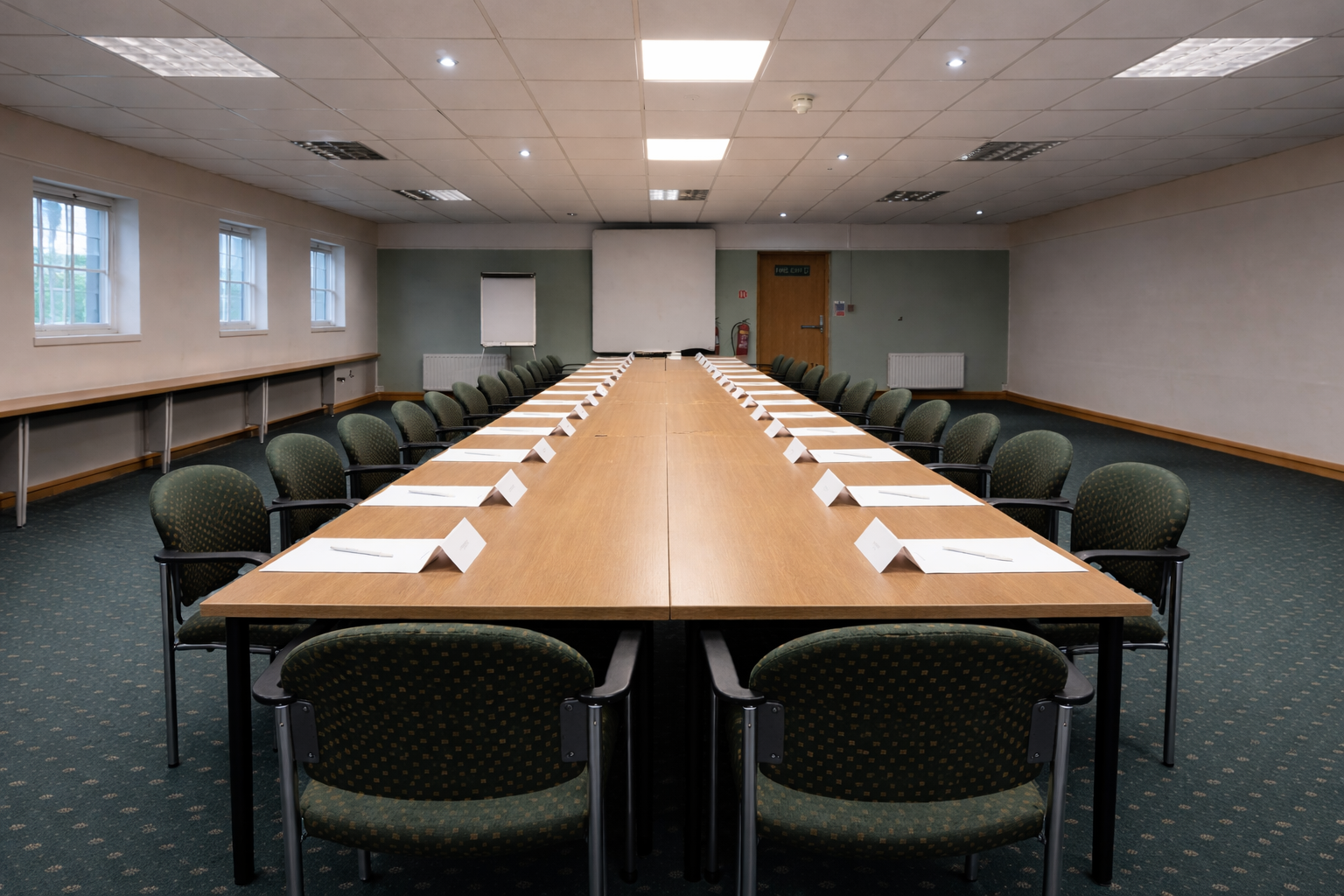 Long table seating 18 in The Congress Room at mercure gloucester bowden hall hotel ready for a meeting, with notepads, bottles of water and bowls of apples on the table